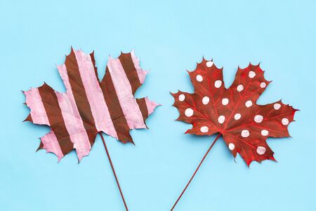 Autumn composition of creative dried leaves maple painted with white striped, polka dots on blue background. Flat lay, top view, copy spaceの写真素材