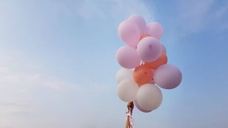 Flying balloons of delicate pink and white coral flowers in female hand on background of blue sky with clouds