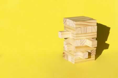 Wood jenga game with wooden block Stack tower on yellow background, manage risk and strategy.の写真素材