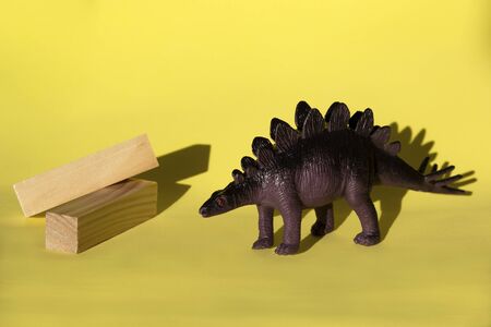 Toy dinosaur Stegosaurus  with wooden beams on yellow background, close-up