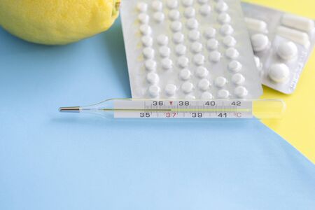 Glass mercury thermometer, lemon and pills, tablets on blue background. Pharmacy theme, treatment and prevention of virus. Concept of health in season of colds.の写真素材