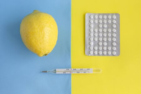 Fresh lemon, pack of tablets and thermometer on blue yellow background. Minimal style in season of...