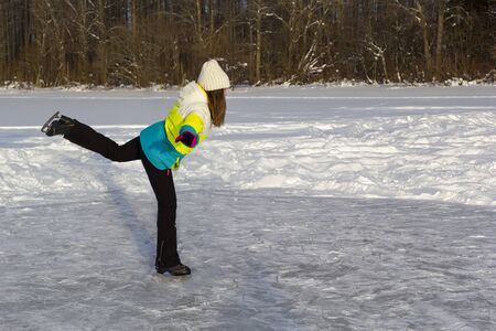 Girl skates on frozen forest lake on sunny frosty day. Makes swallow element.の写真素材