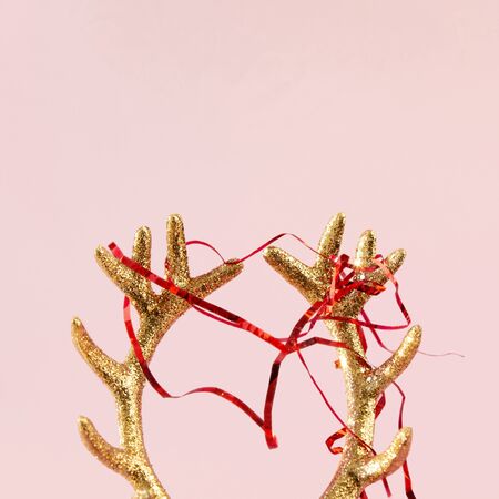 Golden deer horns with red newfoot tinsel on pink background. Xmas composition in minimal styleの写真素材
