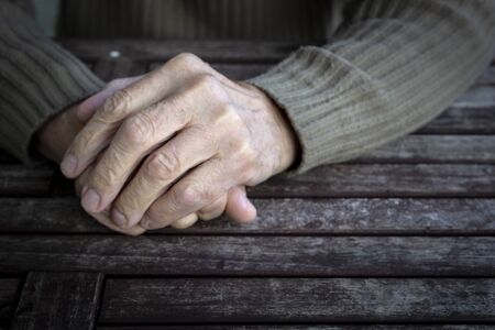 Hands of old senior man with wrinkled palm on wooden table. Copy space, vintage toneの写真素材