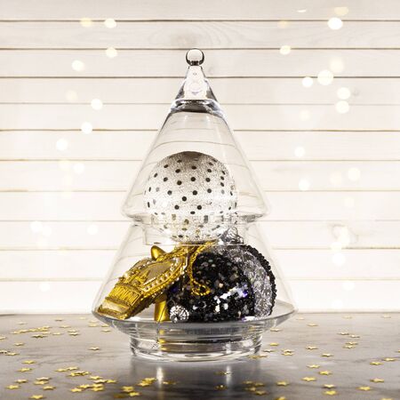 Christmas composition - glass Xmas tree with gold, white and black balls,  bauble and toys with lights on new Year background. Creative greeting card in trend colors, copy spaceの写真素材