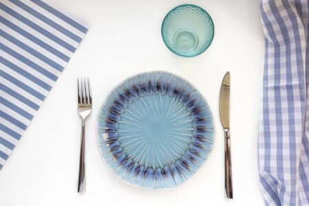 Table set in marine style - blue empty plates, glass, fork and knife on striped napkins. Preparation to table setting. Flat lay, top view, copy spaceの写真素材