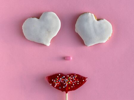 Creative collage of female face made of candy lips and eyes in shape of hearts from cookies on pink...