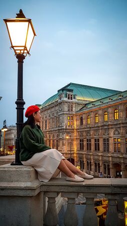 VIENNA, AUSTRIA - NOVEMBER 15, 2019: Romantic girl in red beret admires evening view of city, Vienna Opera in light of street lamps, Vienna, Austriaのeditorial素材