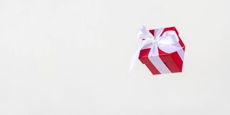 Banner red gift box with white satin ribbon bow flying on white background. Minimal concept for...