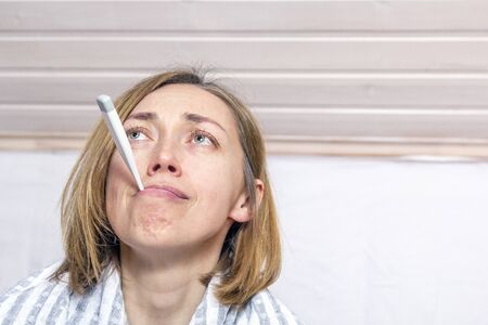 Ill woman with thermometer in mouth on light background. Concept diseases of flu virus, colds, coronavirusの写真素材