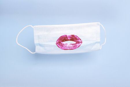 Medical mask with print of female lipstick kiss lips on blue background. Prevention and protection of the population during an epidemic, Corona virus (COVID19), colds and viral fluの写真素材