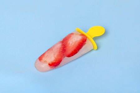 Homemade strawberry frozen juice, ice cream stick on blue background. Bright refreshing taste of...