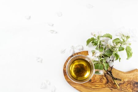 Glass cup of hot green tea with flowering apple tree branch on wooden stand on white background. Top view, flat lay, copy spaceの写真素材