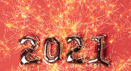 Happy New Year 2021 celebration. Gold balloons in form of numbers with bright sparklers on red background. Flat lay, top view, bannerの写真素材