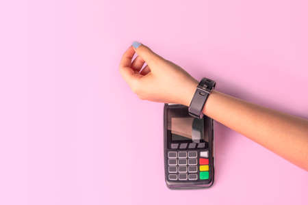 Payment for purchases using smart watches and POS terminal on light pink background. Contactless payment with NFC tecnologyの写真素材
