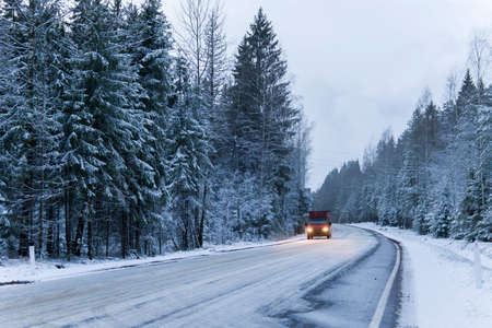 Car drives on empty snowy road in winter forest. Beautiful frosty white landscape at dawn.の写真素材