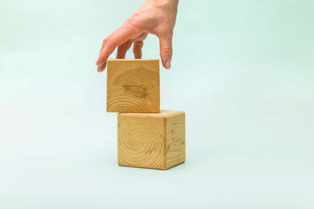 Woman's hand puts blank wooden cube on top of each other. Concept of logical thinking. Abstract creative background with cubes, closeup, copy spaceの写真素材