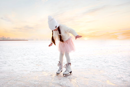 Little girl skating on ice in evening sunset light. Winter sports on natural backgroundの写真素材