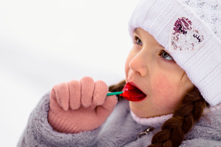 Little girl eating colorful lollipop candy on stick in winter outdoorの写真素材