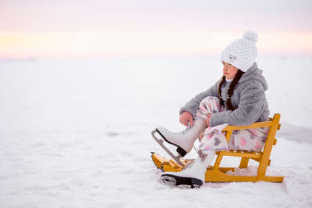 Little girl putting on skates for ice skating in winter outdoor. Winter sports on natural background.の写真素材