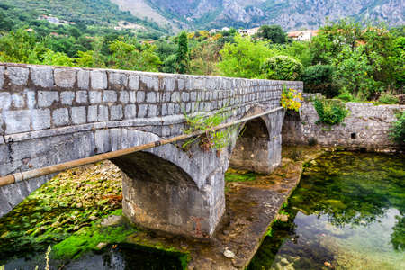 Old stone bridge over small transparent river at foot of mountains, near Risana, Boca-kotor bay, Montenegro.の写真素材