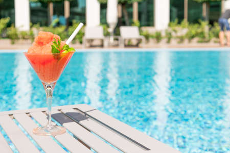 Fresh red cocktail with ice in glass on swimming pool. Tropical juice on luxury vacations. Concept summer holiday and travel.の写真素材