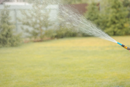 Watering lawn. Irrigation system lawn sprinkler spray water over fresh green grass in garden on summer morning in light outdoors sun with natural blurry background. Close-up, copy spaceの写真素材