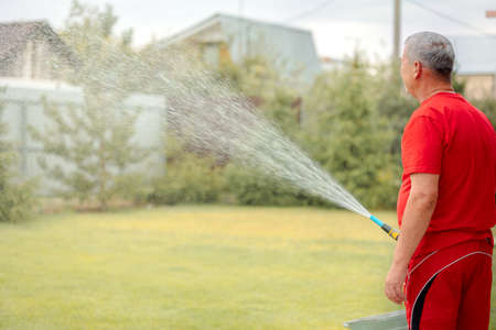 Man watering lawn. Irrigation system lawn sprinkler spray water over fresh green grass in garden on...