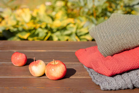Folded autumn and winter clothing. Pile of knitted cashmere sweaters with apple on wooden table....