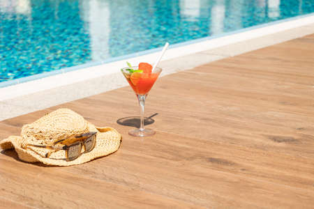 Fresh red cocktail with ice in glass, beach hat and sunglasses on swimming pool. Tropical juice on luxury vacations. Concept summer holiday and travel. High quality photoの写真素材