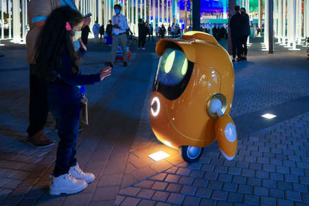 Little girl playing with Opti. Cute small robot mascot in EXPO 2020.のeditorial素材
