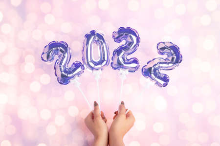 Happy New Year 2022 celebration. Female hands holding golden balloons in form of numbers. Toning in...