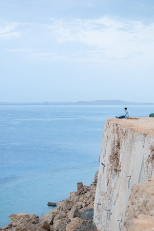 Man greets sunrise of sun on high mountain above sea. Aerial view to calm blue sea with rocky...