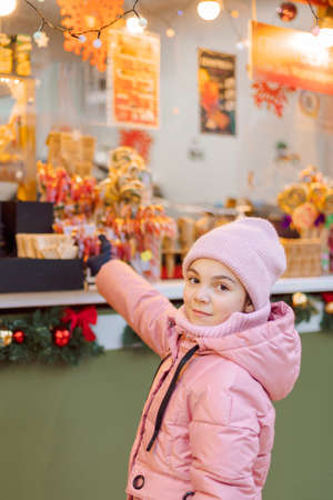 Little happy girl in pink at Christmas fair. People buy gifts for holiday at Christmas marketの写真素材