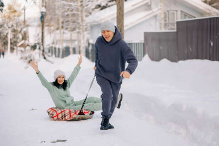 Smiling man giving sledding ride to woman. Love and leisure concept.の写真素材
