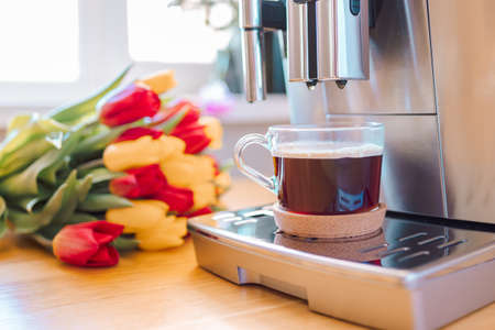 Cup of coffee with milk and tulips flowers on wooden kitchen table. Freshly brewed cappuccino...