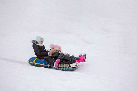 Little girls sledding down hill on walk in winter snowy day. High quality photo