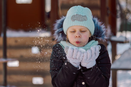 little girl blows snow from her palms on a walk on a frosty winter day. High quality photo