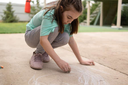 Girl draws with colorful crayons on pavement. Childrens drawings with chalk on wall. Creative kid. Joy of childhood. High quality photoの写真素材