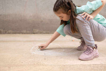 Girl draws with colorful crayons on pavement. Childrens drawings with chalk on wall. Creative kid. Joy of childhood. High quality photoの写真素材
