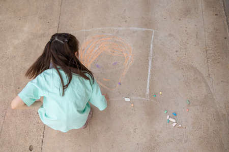 Girl draws with colorful crayons on pavement. Childrens drawings with chalk on wall. Creative kid. Joy of childhood. High quality photoの写真素材