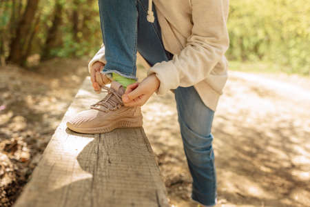 Child tying up laces his sneakers in spring park for walk. Girl ties bow on her shoe outdoors. Health and sport concept. High quality photoの写真素材