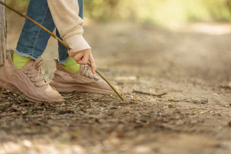 Little girl paints draws on ground with stick in open air in spring blooming fairytale park. High...