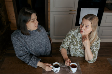 Two women talking at home. Girlfriends drinking cup of coffee in kitchen. High quality photo