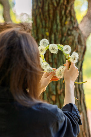 Happy girl with wreath of white dandelions on green lawn on summer sunny day. High quality photoの写真素材