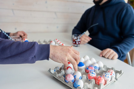 Two men are playing chess with Easter eggs at white table. Creative ideas for unusual chess. Colorful painted egg figures. High quality photoの写真素材