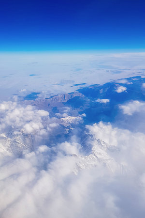 View from window of plane to blue sky and snowy mountain peaks in white clouds. high quality photo