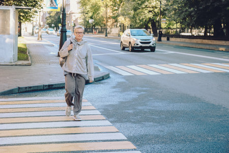 Woman crossing street at crosswalk. Beautiful blonde hair girl cross road street. City lifestyle portrait. High quality photoの写真素材