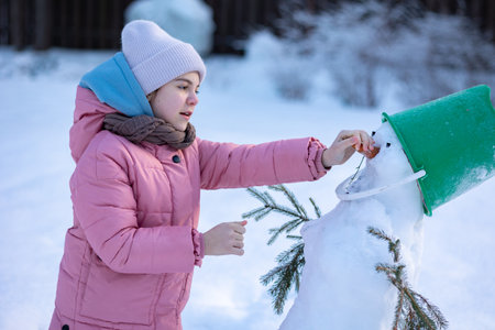 Little girl makes snowman on winter frosty day. Child makes nose out of carrot. . High quality photoの写真素材